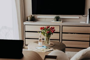 Ein Wohnzimmer mit rundem Couchtisch, einem flachbildfernseher an der Wand, einem Bücherregal und einem Fenster mit Vorhängen.