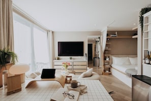 A modern living room with a flat-screen TV, a sofa, a coffee table with books and a laptop, and a dining area with a table and chairs. - Saturn Studio by Navie Stays (Poole)