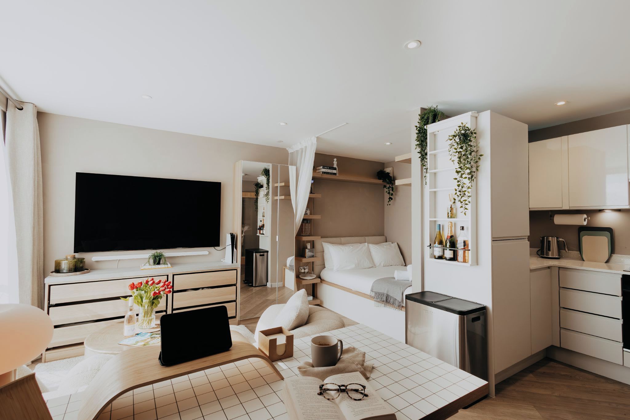 A modern apartment with a flat-screen TV, a dining area with a table and chairs, a kitchen with white cabinets, and a living area with a sofa and a bed.