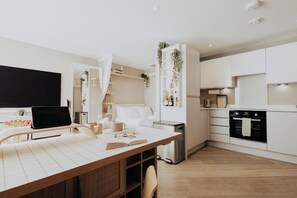 A modern kitchen with white cabinetry, a dining area with a wooden table, and a black TV on a stand. - Saturn Studio by Navie Stays (Poole)