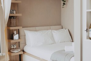 Ein ordentlich bezogenes Bett mit weißen Leinen, ein Nachttisch mit Taschentuchbox und ein Regal mit Büchern und einem Schild.