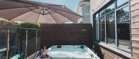 A hot tub with a wooden deck, a glass enclosure, and a large umbrella.