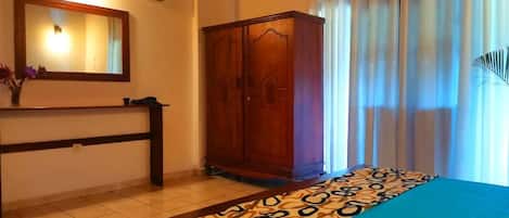 A bedroom with a bed, a wooden wardrobe, a mirror, and a window with curtains.