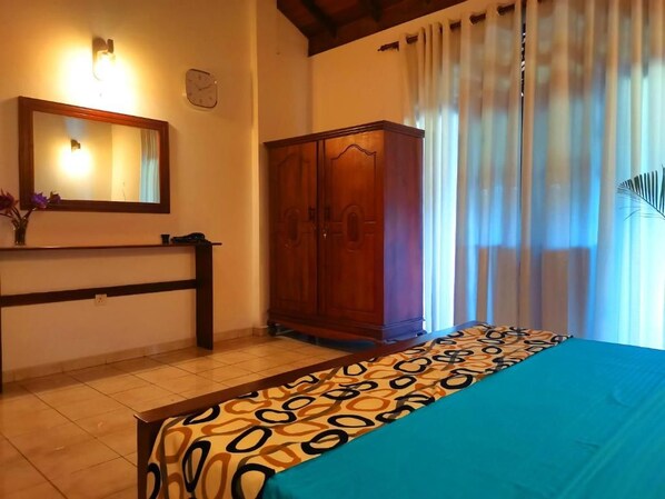A bedroom with a bed, a wooden wardrobe, a mirror, and a window with curtains.