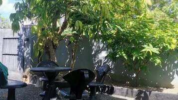 Un espacio al aire libre con mesas y sillas, rodeado de árboles y una pared.