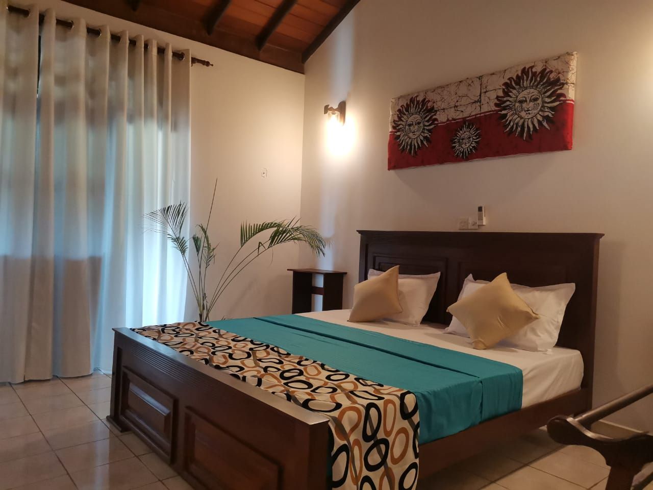 Un dormitorio con cama, mesita de noche, lámpara de pared y una obra de arte decorativa con un motivo de sol.