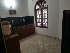 A kitchen with a tiled floor, wooden cabinets, a black countertop, a water dispenser, a decorative window, and a wall-mounted light fixture.