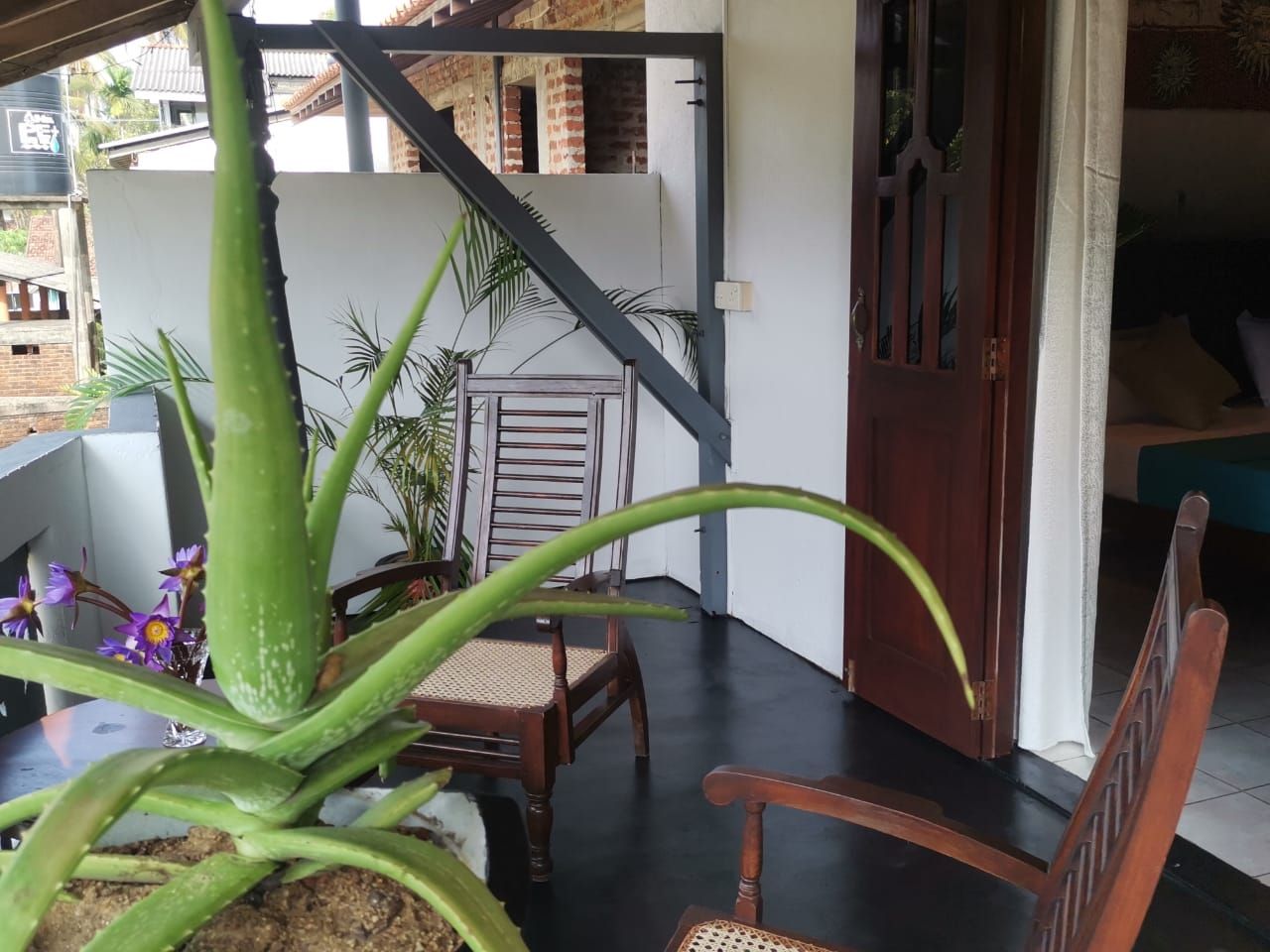A balcony with a wooden chair, a table, and a potted aloe vera plant.