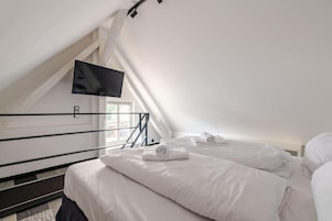 Habitación de hotel con dos camas, un televisor de pantalla plana montado en la pared y un ventanal que proporciona luz natural.