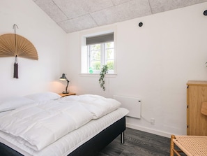 Ein Schlafzimmer mit Bett, Nachttischlampe, Fenster, Heizkörper und einem Holzschrank.