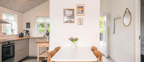 A modern kitchen with a dining area, featuring a white table, wooden chairs, and a vase with flowers.