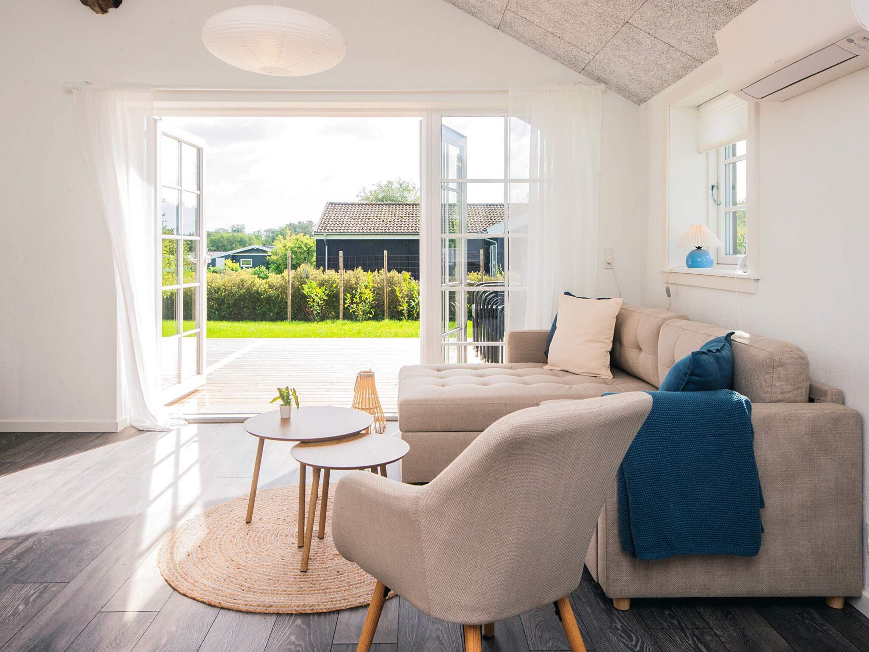 A modern living room with a sofa, a round table, and a view of a house through large windows.