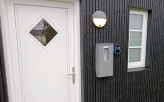 A white door with a diamond-shaped window, a wall-mounted light fixture, and a small electrical box with a cable.