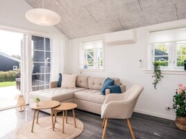A modern living room with a sectional sofa, two round wooden tables, and a hanging light fixture.