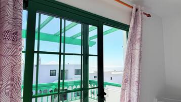 Une pièce dotée d’une grande fenêtre, d’une porte à cadre vert et offrant une vue sur des immeubles et un ciel dégagé.