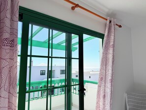 Quarto com uma janela grande, porta com moldura verde e vista para edifícios e céu claro.