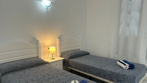 Een hotelkamer met twee éénpersoonsbedden, een nachtkastje met een lamp en een raam met gordijnen.