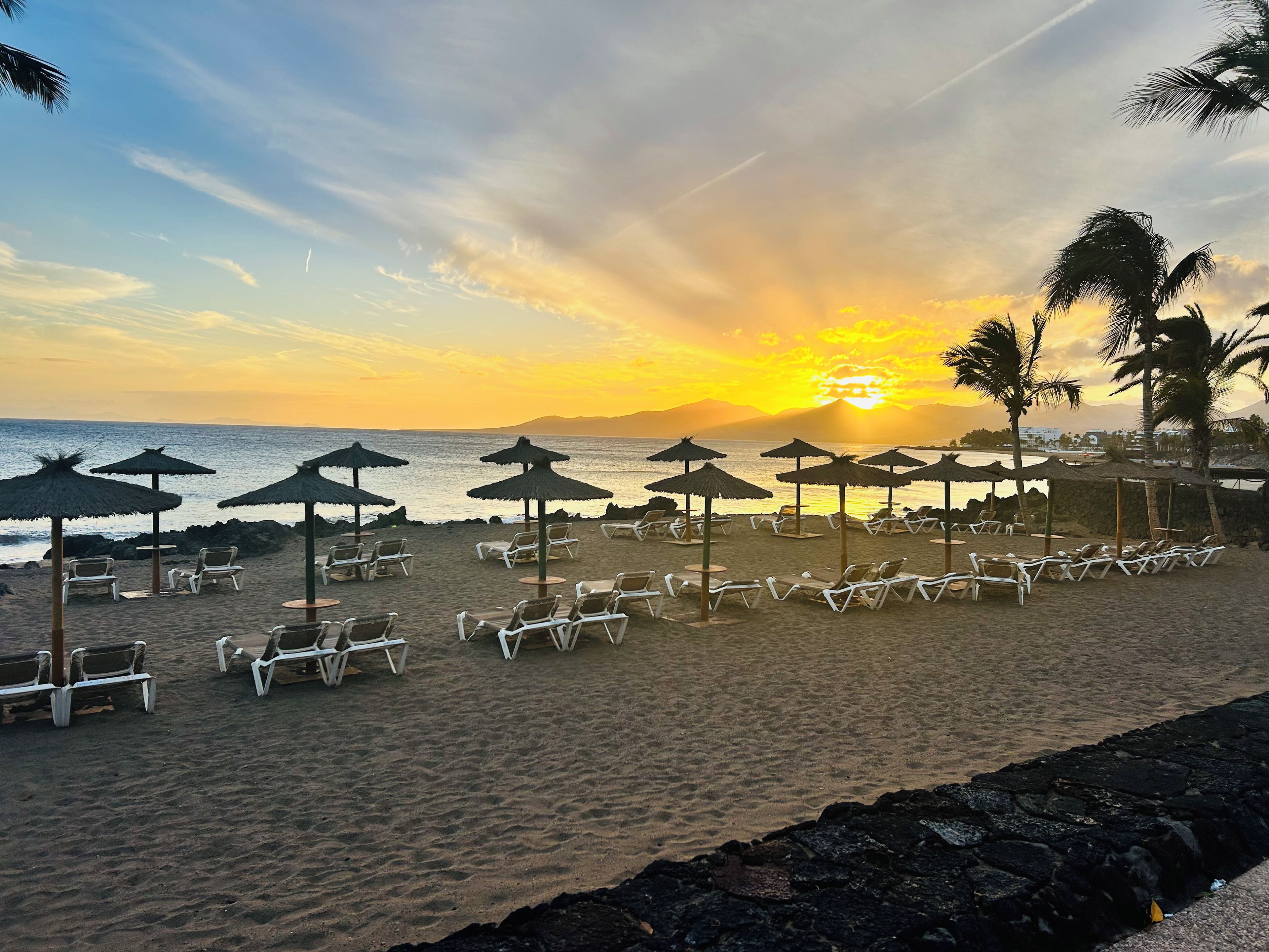 Une plage avec des transats et des parasols, un ciel dégagé et un coucher de soleil.