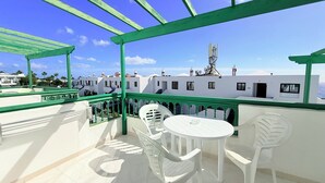 Een balkon met een witte tafel en stoelen, groene leuningen en een uitzicht op gebouwen op de achtergrond.