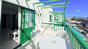 Een balkon met een witte tafel en stoelen, een groene reling en een helder uitzicht op de straat.