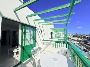 En balkon med et hvidt bord og stole, gelænder i grøn farve og frit udsyn til gaden nedenfor.