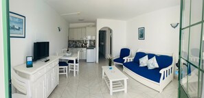 Um espaço compacto com cozinha compacta, área de refeições, sofá e televisão.