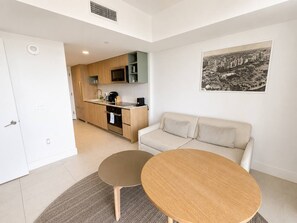 Ein modernes Wohnzimmer mit einer Couch und einem runden Tisch, eine Küche mit Holdekor und ein Stadtbild an der Wand.