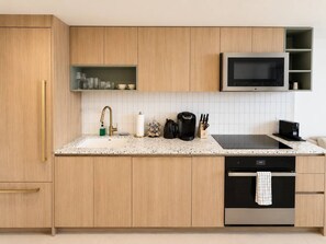 A modern kitchen with wooden cabinets, a granite countertop, a built-in microwave, and a stainless steel oven. - 38th Floor 1 Bedroom Apartment with balcony & bay views in Downton Miami (Miami)