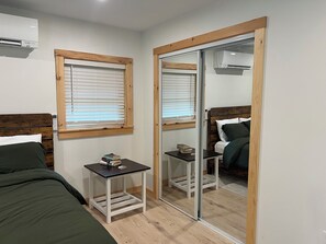 A bedroom with a bed, a bedside table with books, a mirror, and an air conditioning unit. - Private River Creek Retreat In White Mountains. Pet Friendly! (Wentworth)