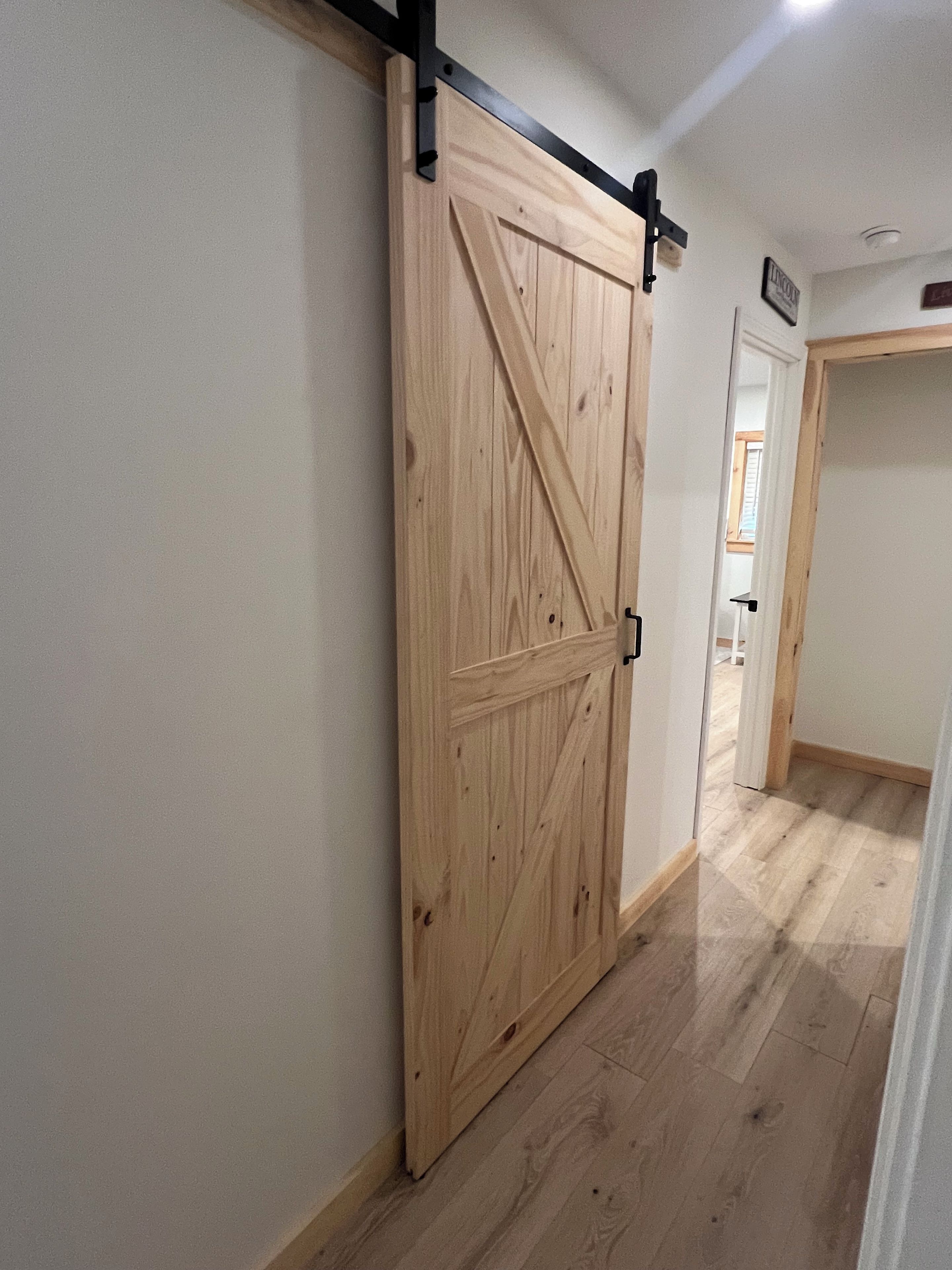 Une porte coulissante en bois, dotée d’une poignée noire, qui donne sur une pièce au plancher de bois et aux murs blancs.
