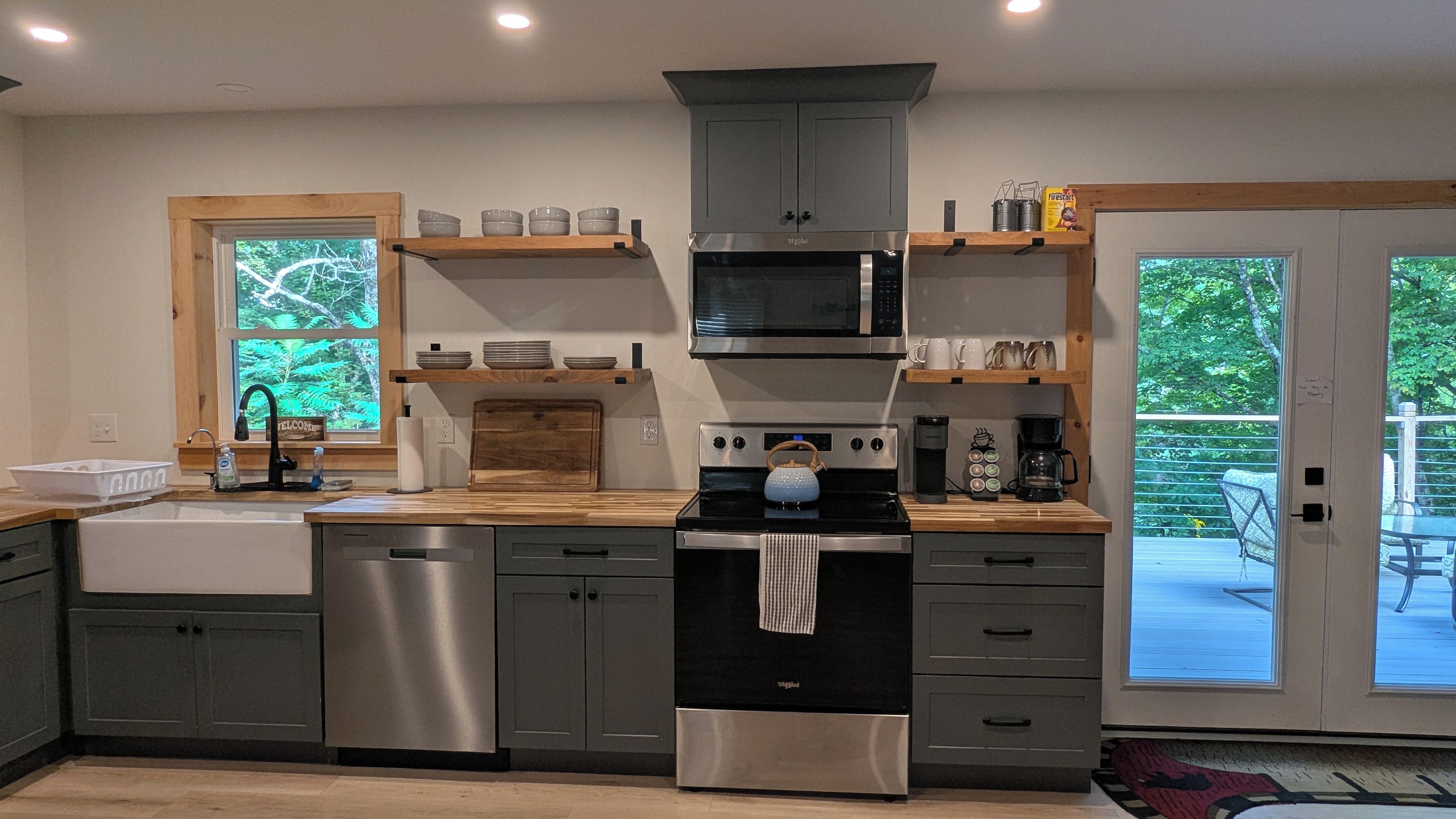 A modern kitchen with stainless steel appliances, wooden shelves, and a view of the outdoors.