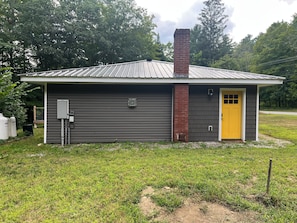 A small building with a metal roof, a brick chimney, and a yellow door.