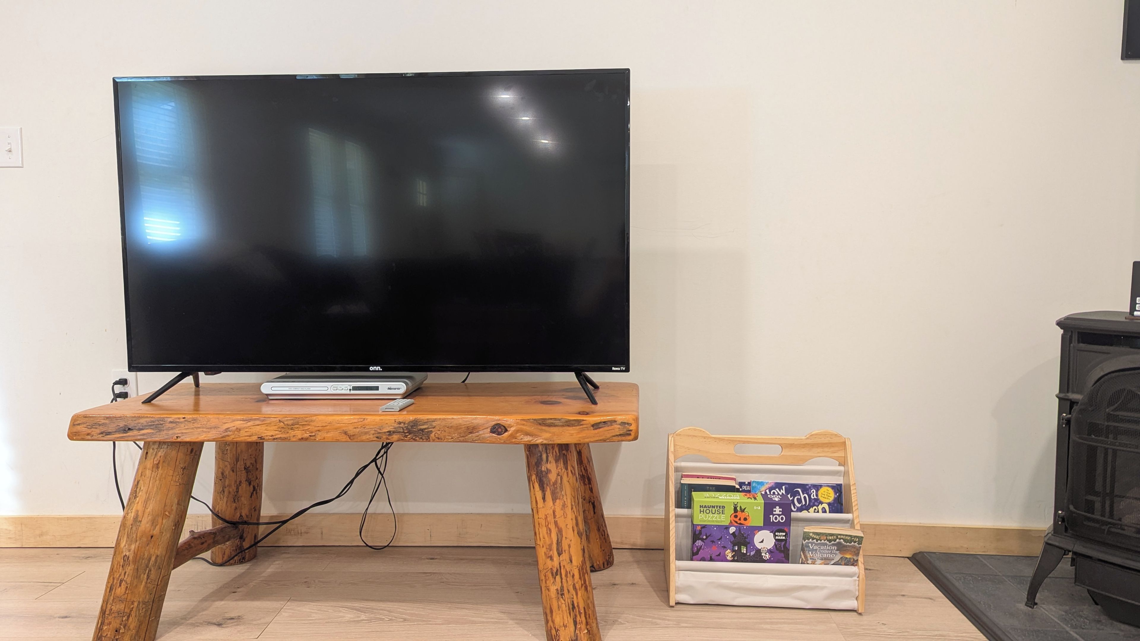 A flat-screen TV on a wooden stand with a remote control, a DVD player, and a small white bag with books and puzzles.