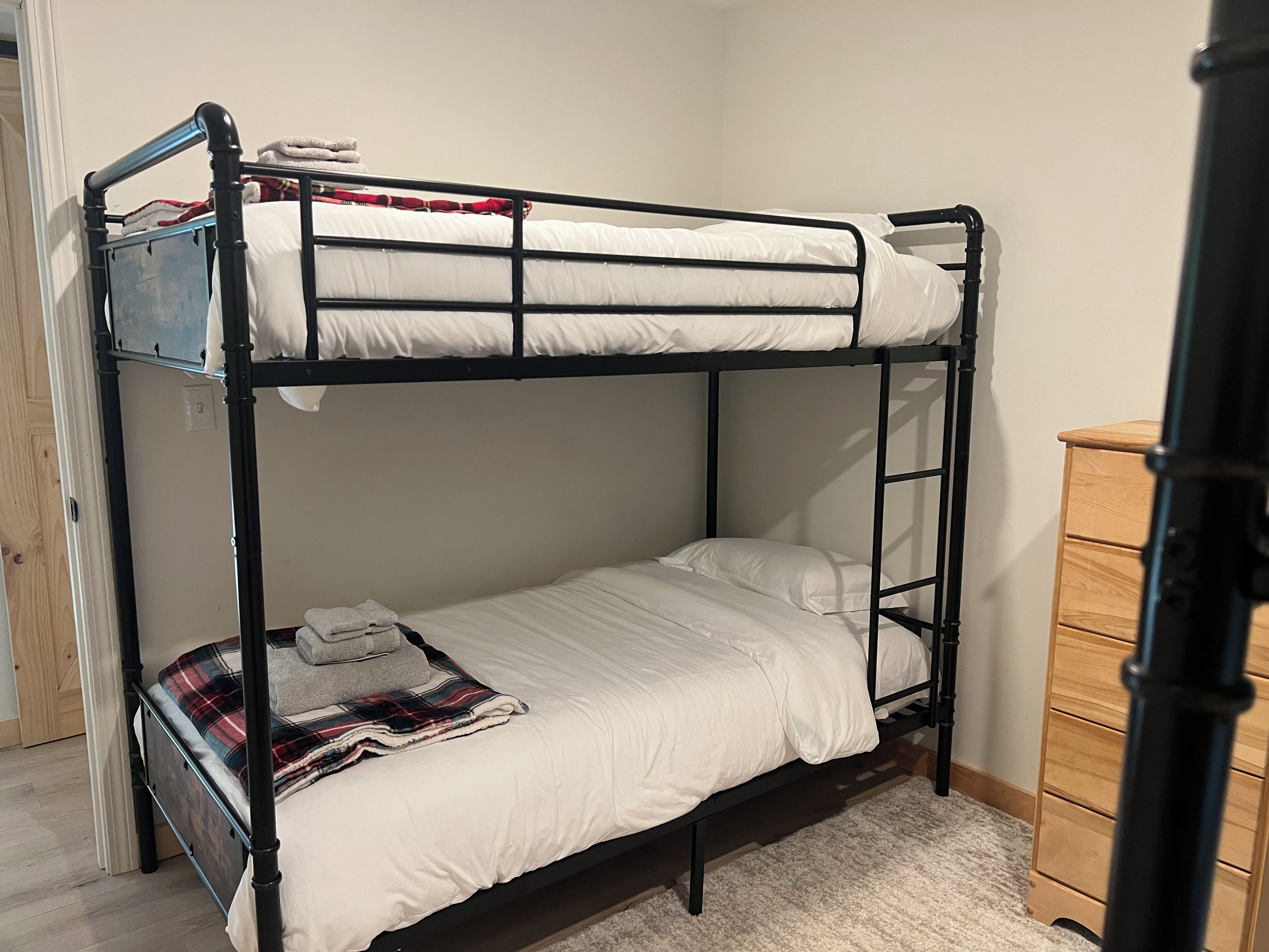 A bunk bed with white bedding and a plaid blanket on the lower bunk.