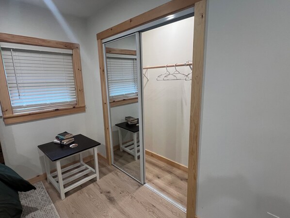 A small room with a wooden-framed sliding door closet, a small table with books, and a window with blinds.