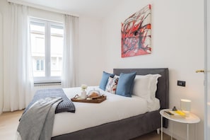 Ein modernes Schlafzimmer mit einem großen Bett, einem Nachttisch, einem Beistelltisch und einem Fenster mit Vorhängen.