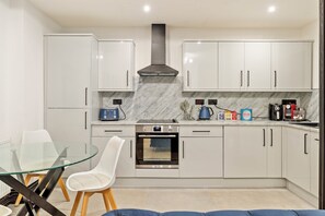 A modern kitchen with white cabinets, a built-in oven, and a glass dining table with chairs. - 1 Bedford House - Close to Town and Seafront (Tenby)