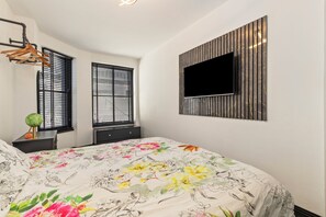 A bedroom with a bed, two windows with blinds, a mounted TV, and a wall-mounted shelf. - 1 Bedford House - Close to Town and Seafront (Tenby)