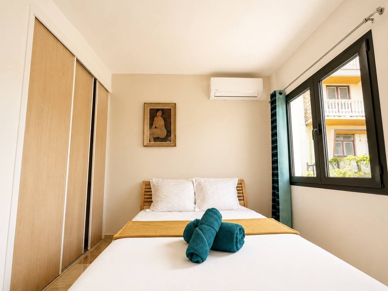 Quarto de hotel com cama, janela, ar condicionado e um quadro na parede.
