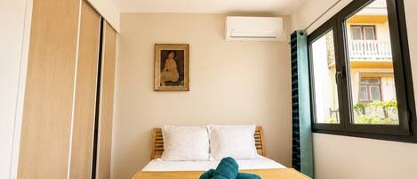 Ein Hotelzimmer mit Bett, Fenster, Klimaanlage und einem Gemälde an der Wand.