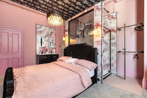 A bedroom with a bed, a vanity with a mirror, a chandelier, and a wardrobe. - 2 Bedford House - Close to Town and Seafront (Tenby)