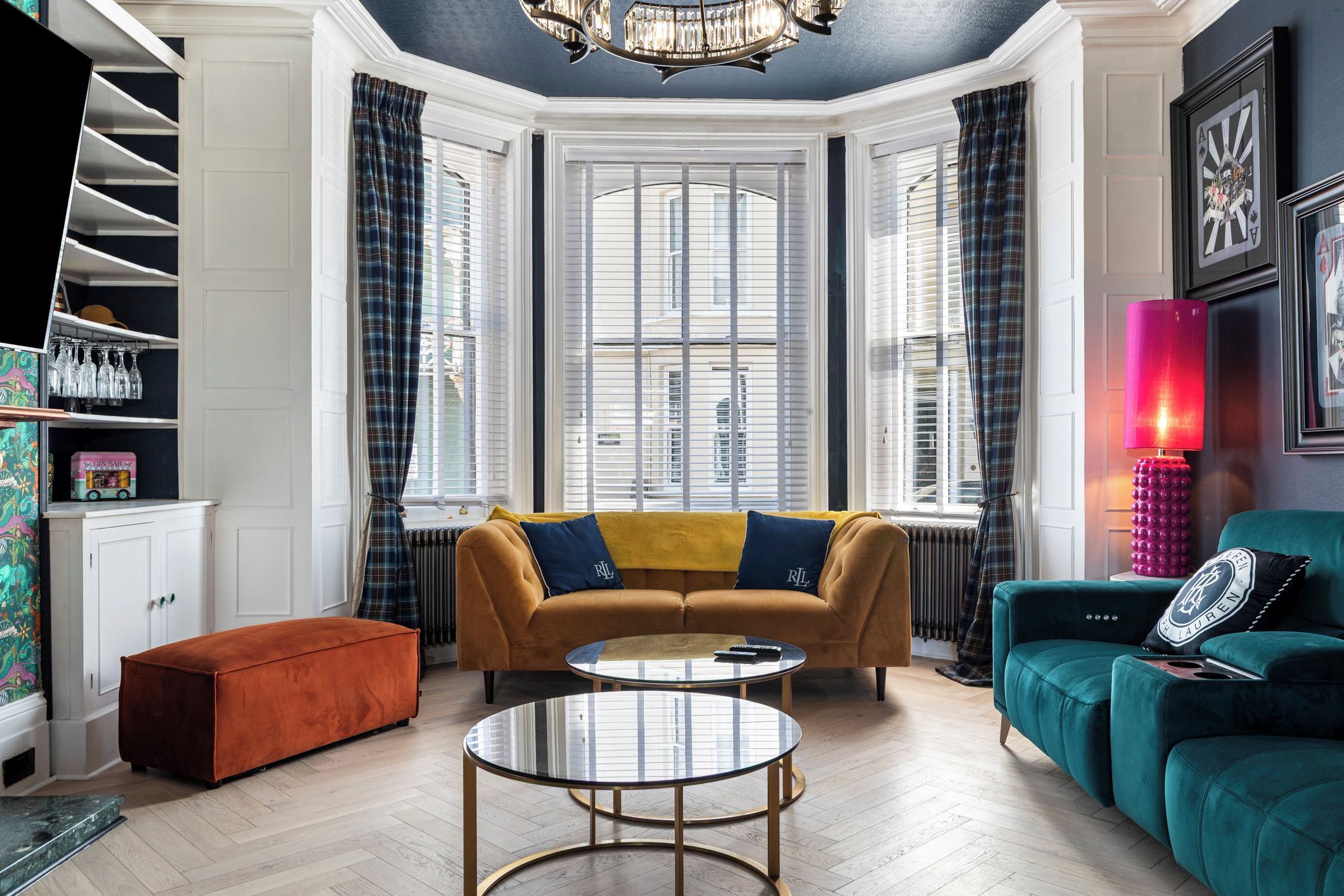 Un salon comprenant un canapé, un pouf, une table basse et donnant sur la rue grâce à de grandes fenêtres.