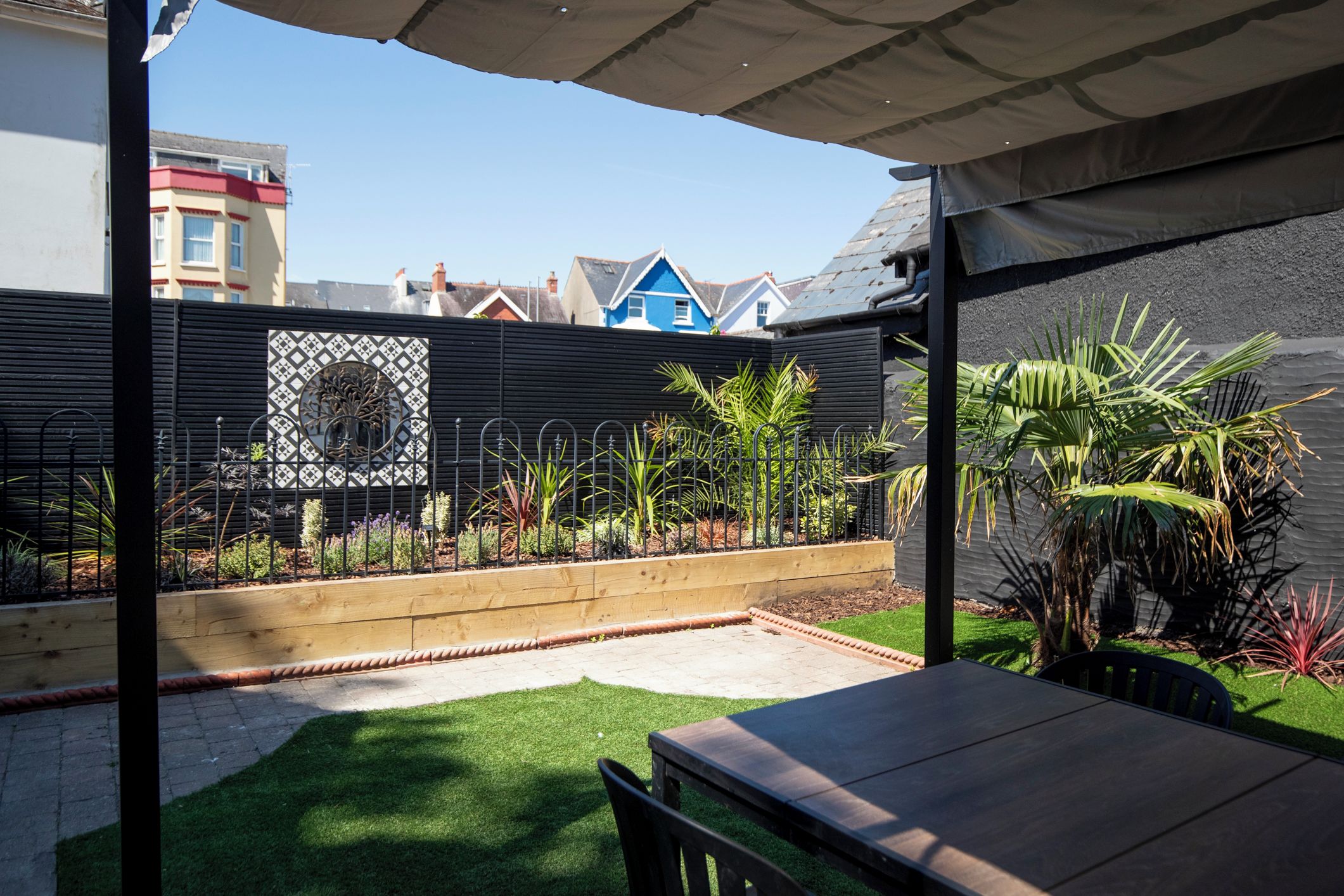 A patio area with a table and chairs, a small lawn, and a decorative metal fence.