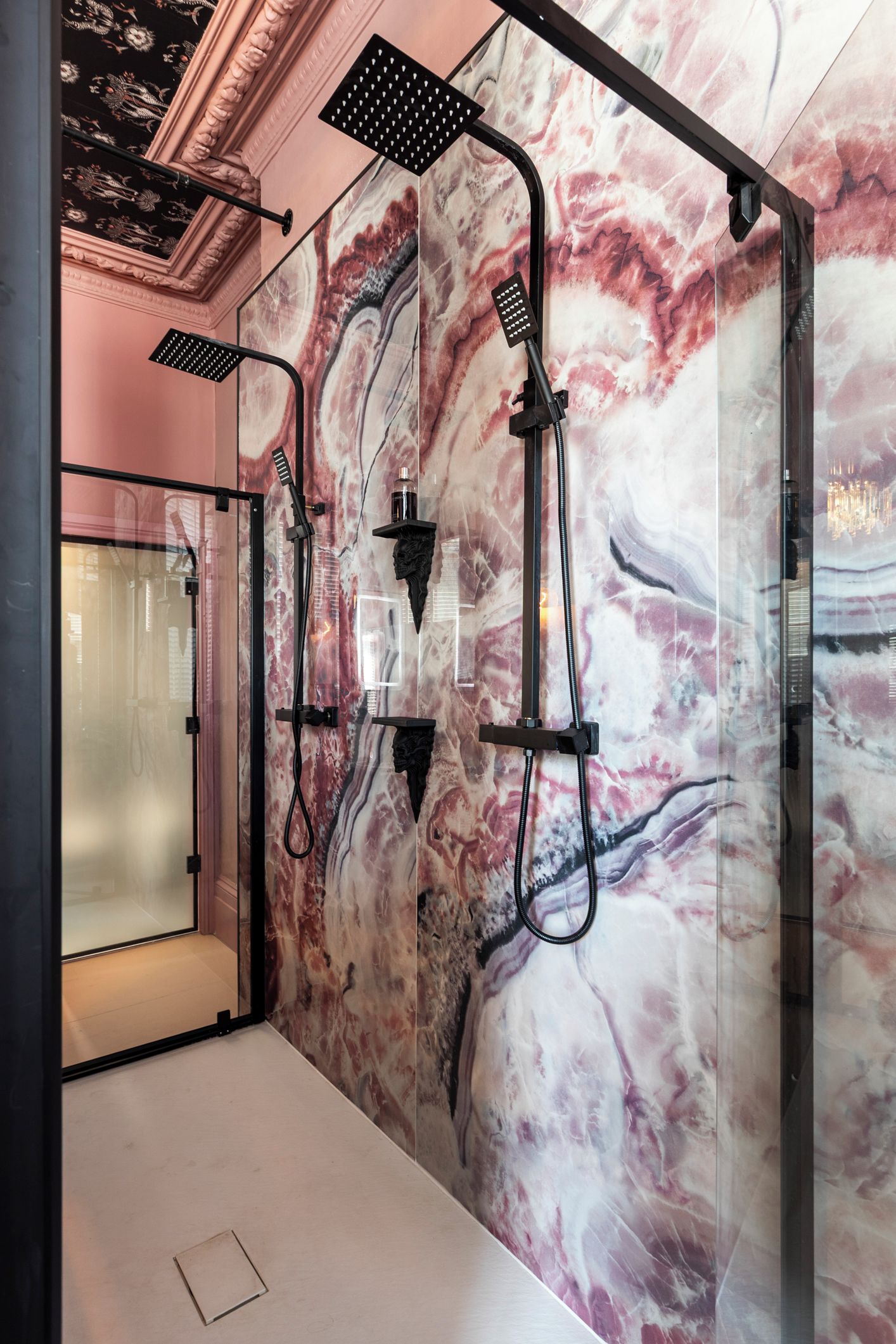 A modern bathroom with a marble wall, a glass shower enclosure, and a black showerhead.