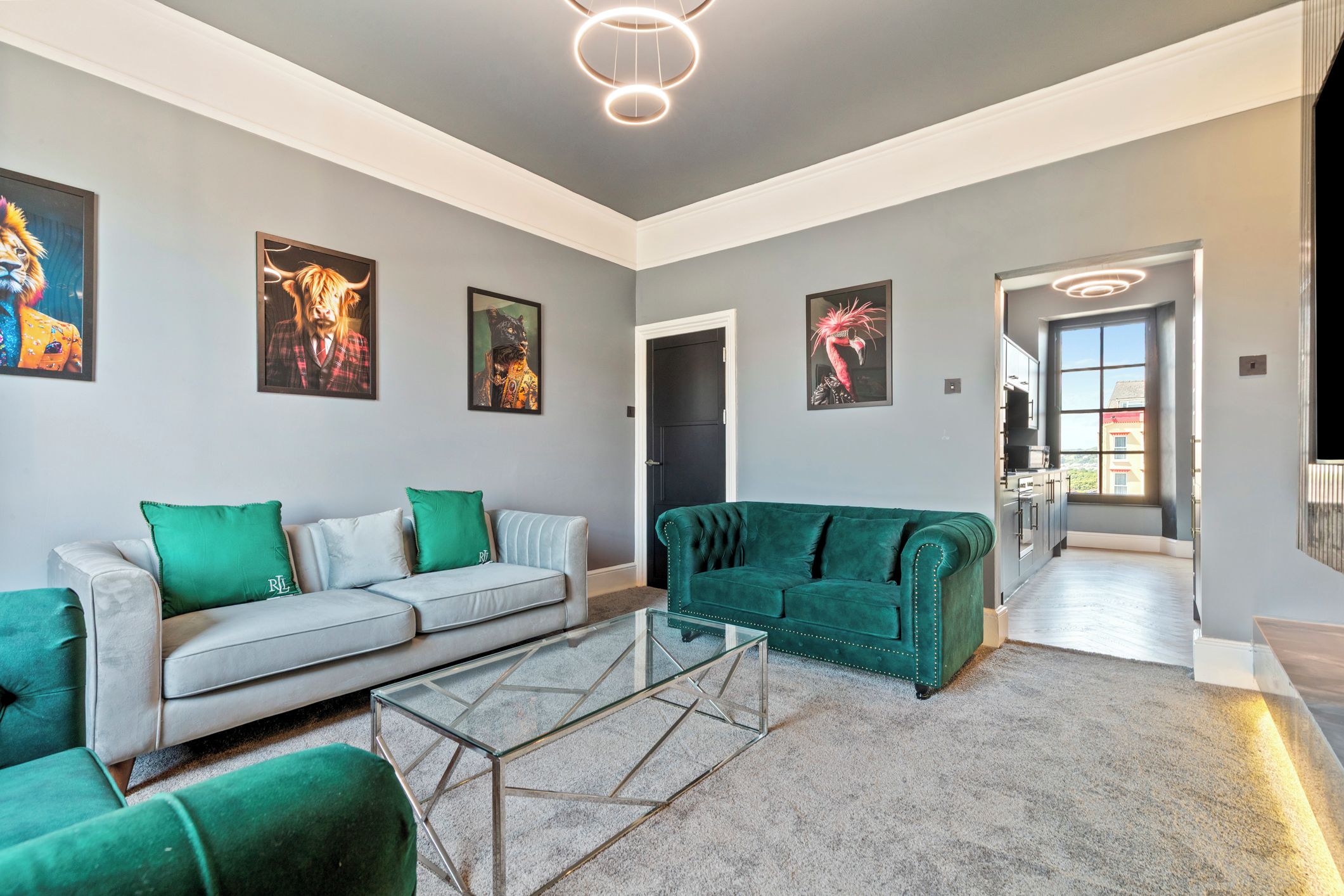 Un salón amplio con un sofá gris, un sofá verde y una mesa de centro de vidrio.