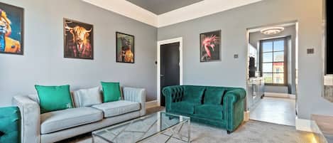 A spacious living room with a grey sofa, a green sofa, and a glass coffee table.