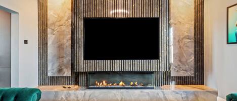 A modern living room with a large flat-screen TV mounted above a fireplace, flanked by marble-like panels, and a carpeted floor.