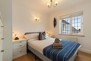 Ein Schlafzimmer mit einem Bett, Nachttischen, einem Fenster und einer Wandleuchte.