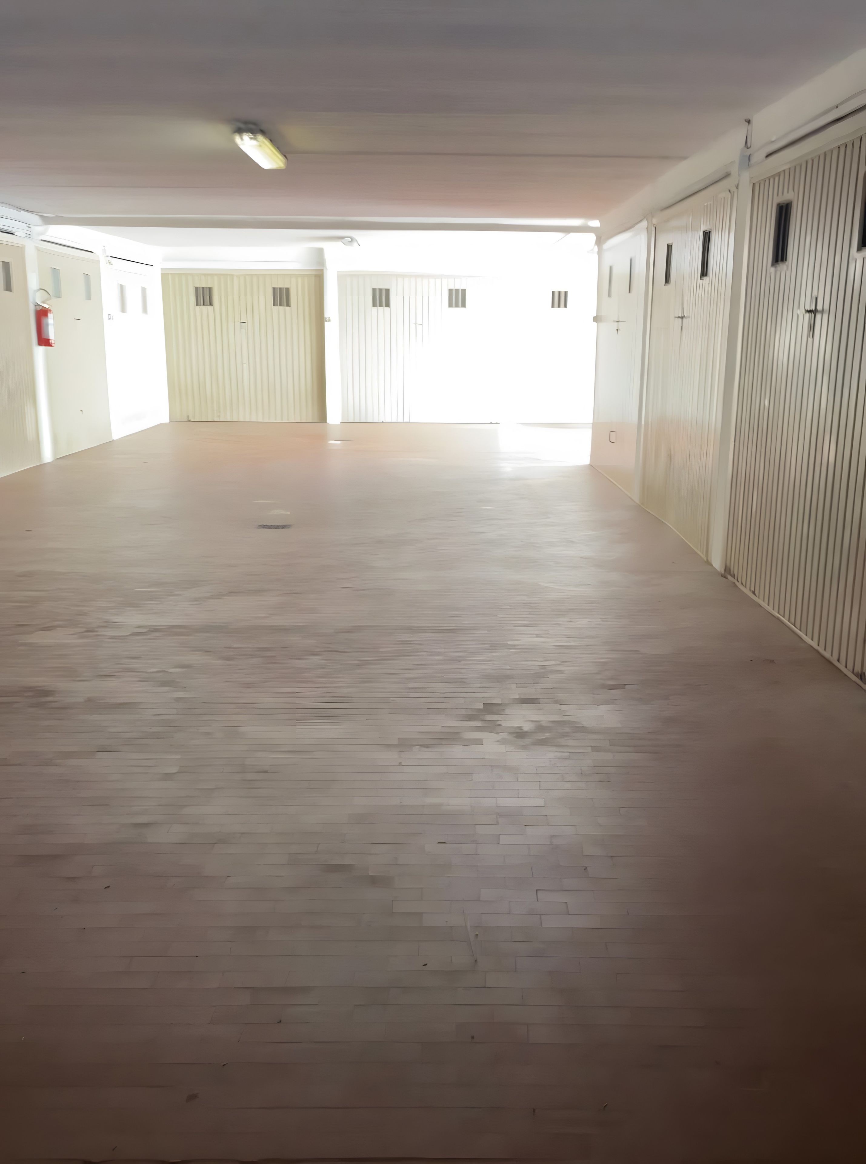 A spacious corridor with a wooden floor, white walls, and a series of doors on one side.