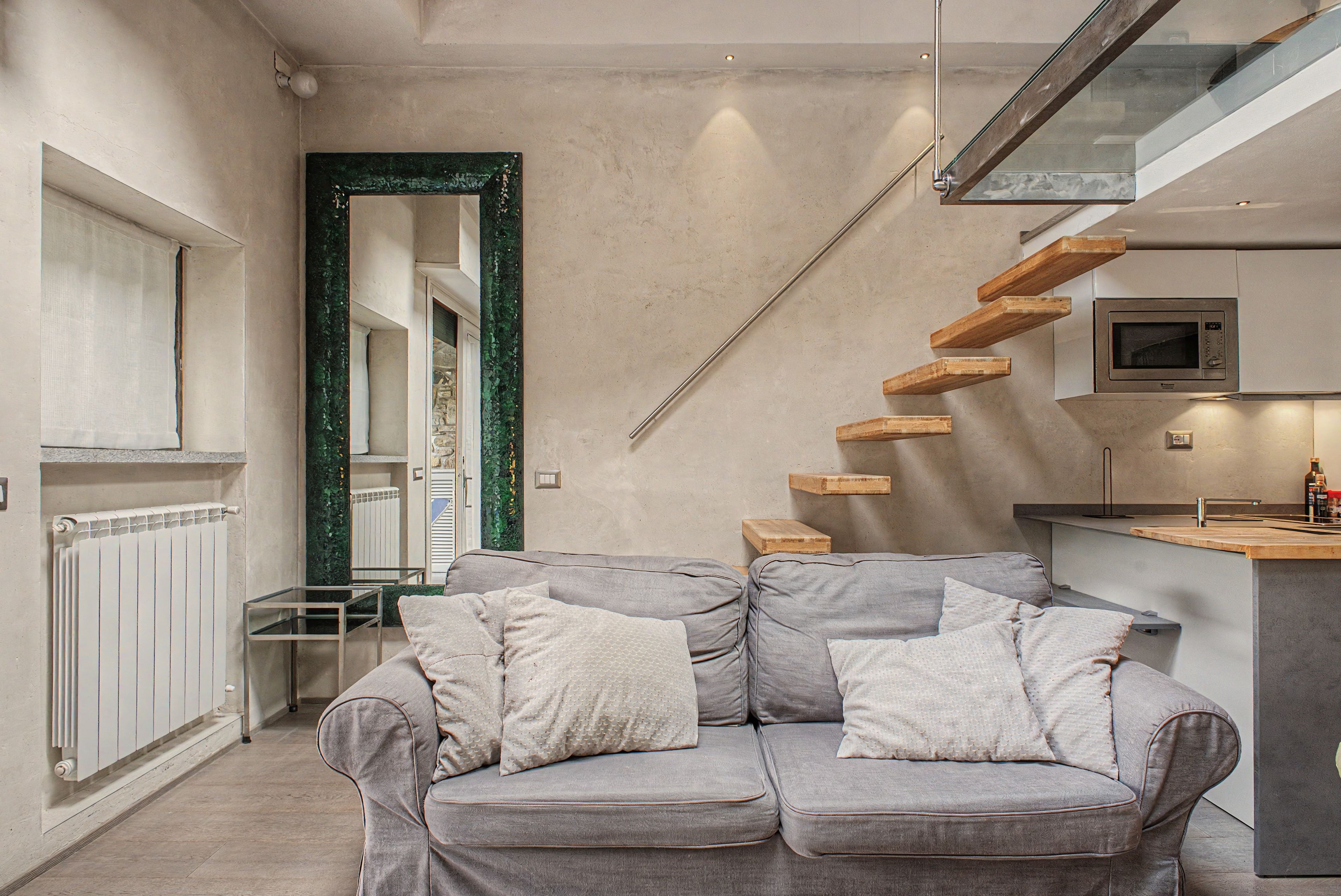 A modern interior with a grey sofa, wooden staircase, and a kitchen area.